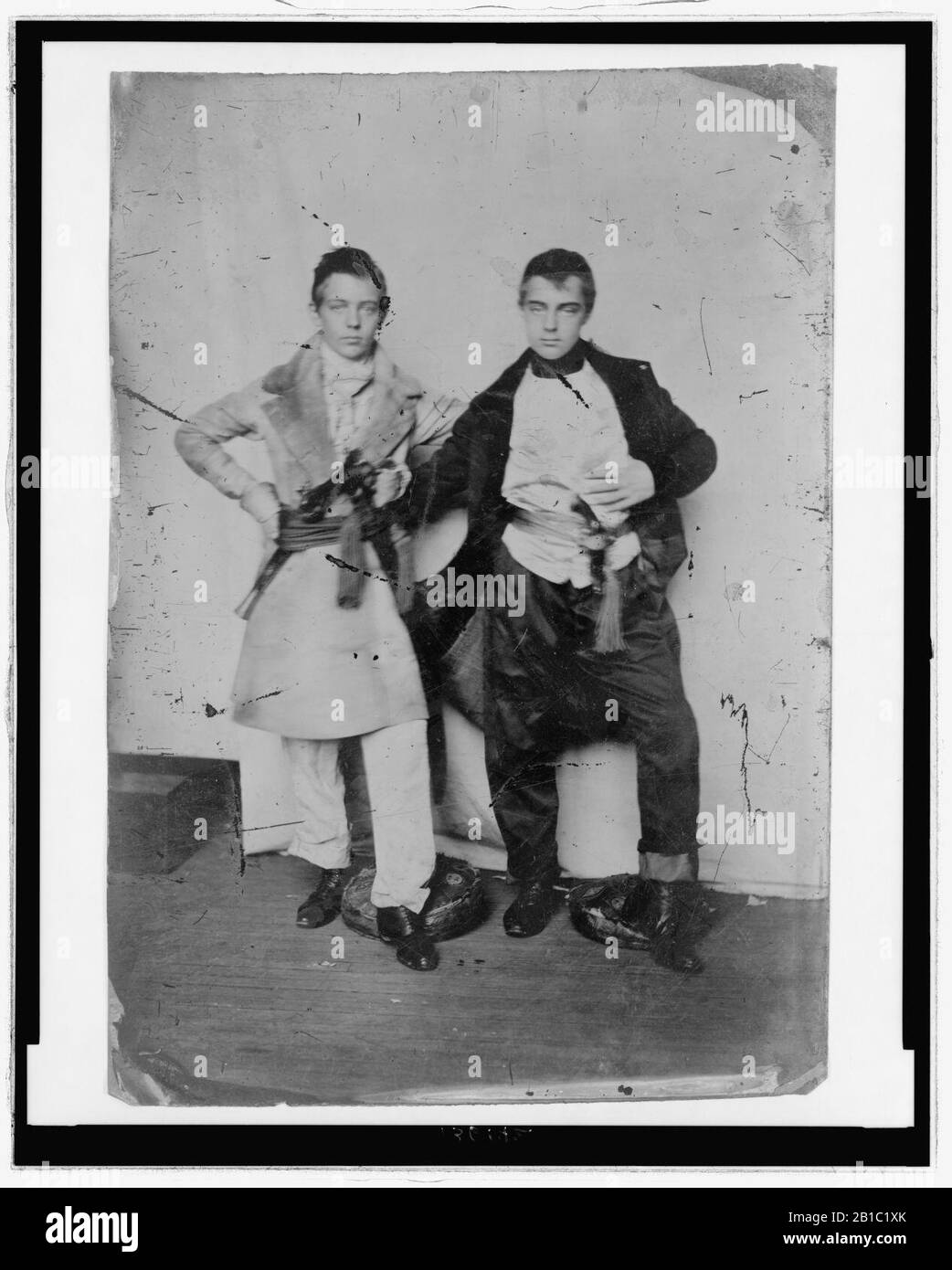 Durchgesicktes Porträt zweier junger Männer, die an ihren Waisten mit fröckigen Mänteln mit Strichen und Pistolen bekleidet sind Stockfoto