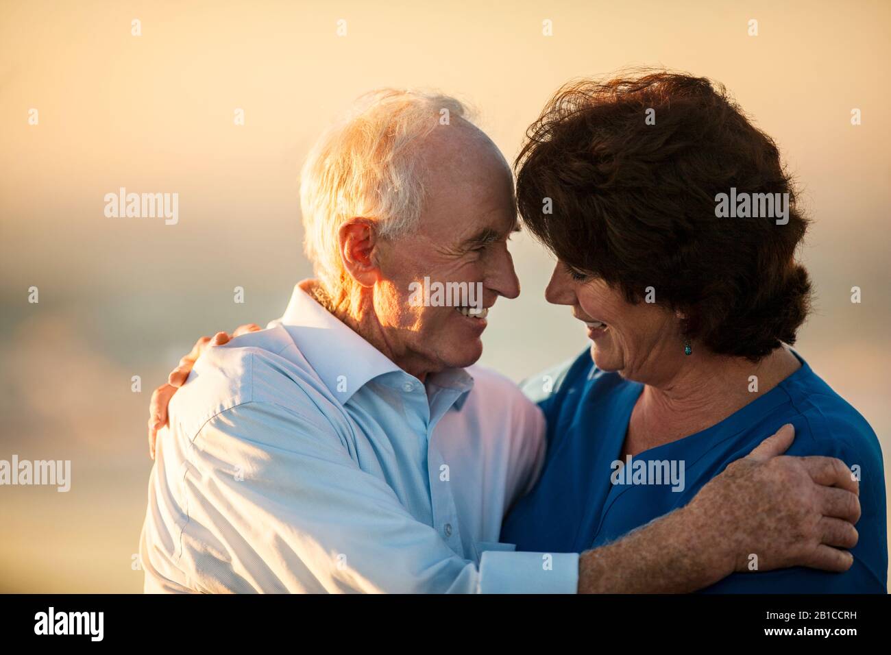 Lächelnder älterer Mann, der eine Krankenschwester im Sonnenschein umarmte. Stockfoto