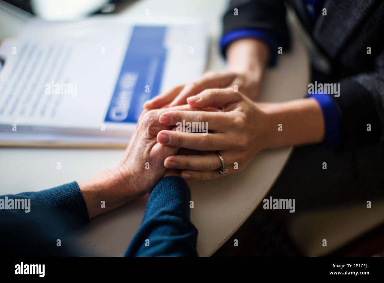Hände von mittleren Erwachsenen und älteren Frauen halten sich gegenseitig auf einem Tisch. Stockfoto