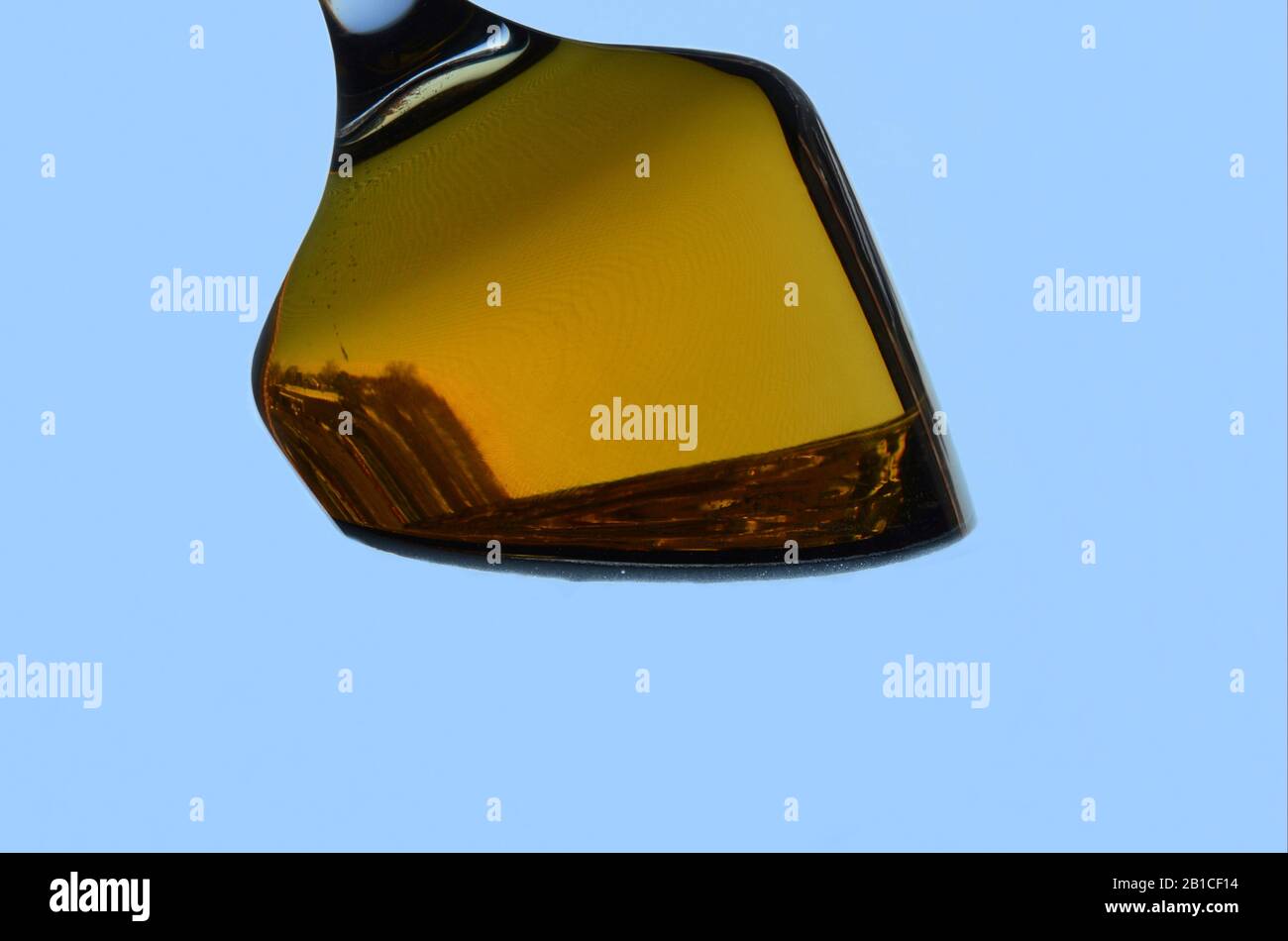 PENDEL: Ein Glas Bier durchläuft eine ungewöhnliche Gravitationstransformation vor blauem Hintergrund. Stockfoto