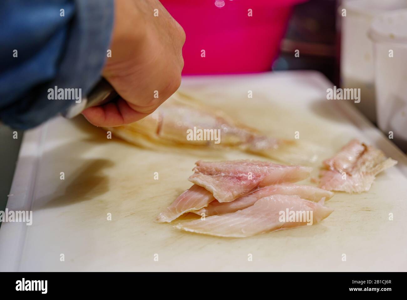 In Scheiben geschnittene Fischfilets und verwischter Hintergrund von Chef'Hand verwenden Messer zum Schneiden und Schneiden von rotem Snapperfisch auf weißem Hackblock in der Küche. Stockfoto