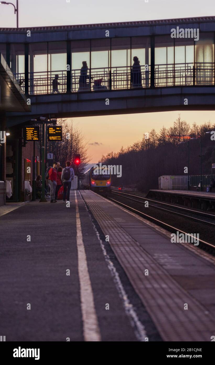 Erster Zug der Transpennine Express-Klasse 185, der am Autobahnkreuz Meadowhall bei Sonnenuntergang mit Passagieren auf dem Bahnsteig und der Fußgängerbrücke abfährt Stockfoto