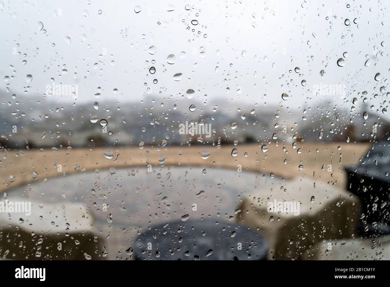 Blick von innen auf eine Bergkuppe einer Terrasse und Unterteilung unten, wenn Regen fällt. Durch ein mit Regen bedecktes und von Wasser beschmutztes Fenster geführt. Stockfoto