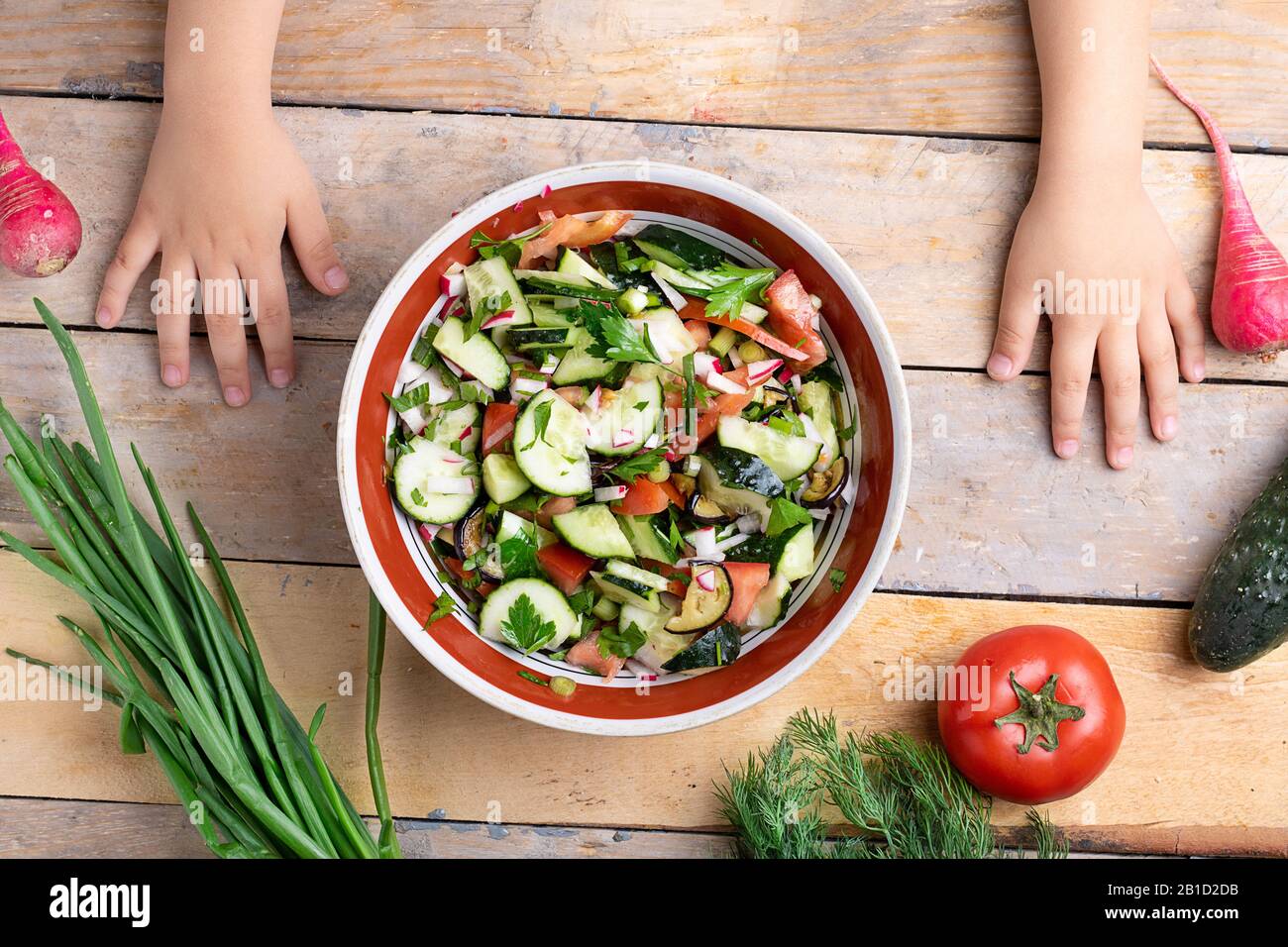 Kinder bereiten frischen gesunden Salat in der Nähe von verschiedenen Gemüse- und Obstsorten auf Holztisch vor, flacher Lay Stockfoto