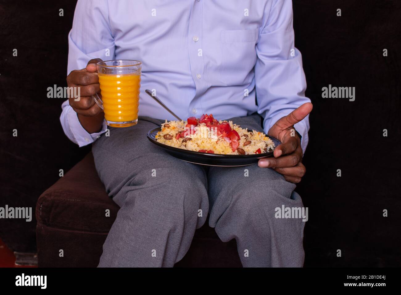Unerkannter afrikaner, der ein Glas Saft mit seinem Essen auf dem Schoß hält Stockfoto