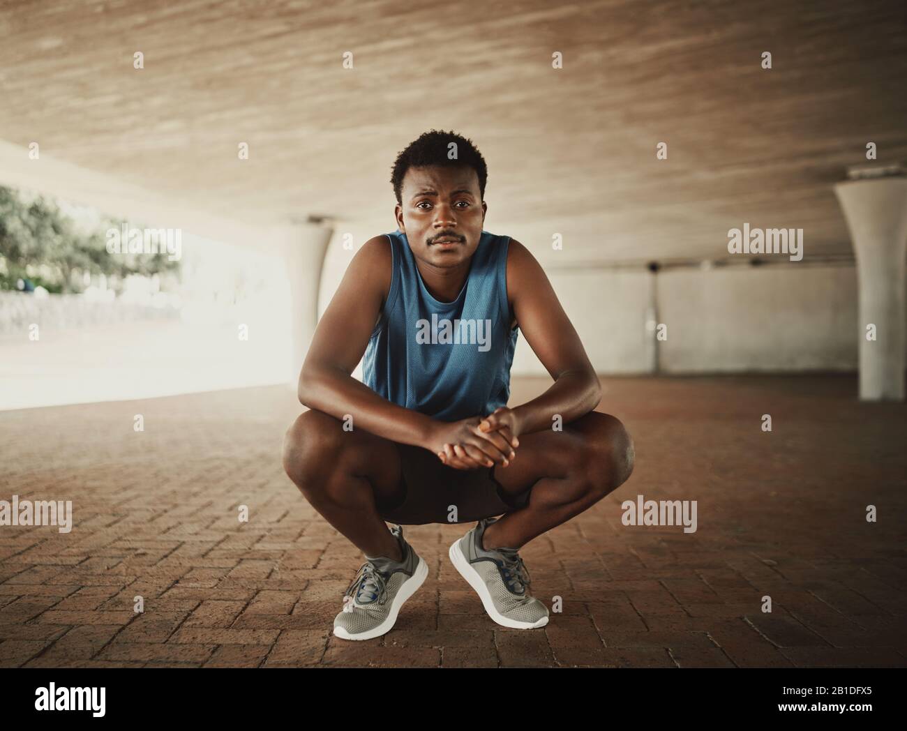 Portrait eines Fitness-Läufers in Sportswear, der auf dem Straßenbelag kaut und auf die Kamera blickt Stockfoto