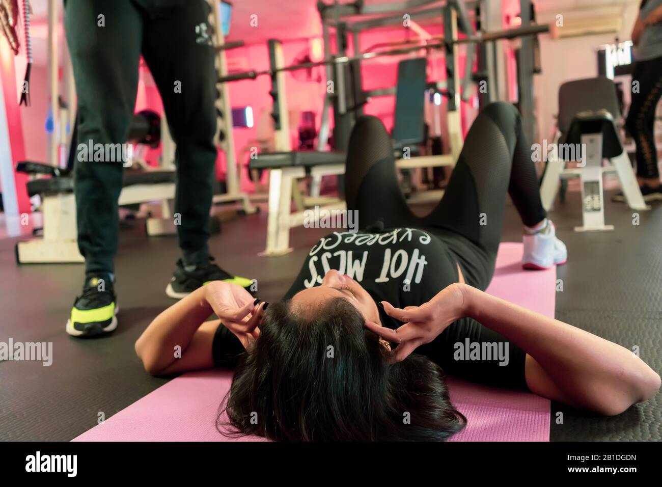 Trainer hilft jungen Frauen, Bauchübungen im Hintergrund von Fitnessbällen zu machen. Schöne Frau macht abs auf einer Matte und ein Mann hilft ihr dabei Stockfoto