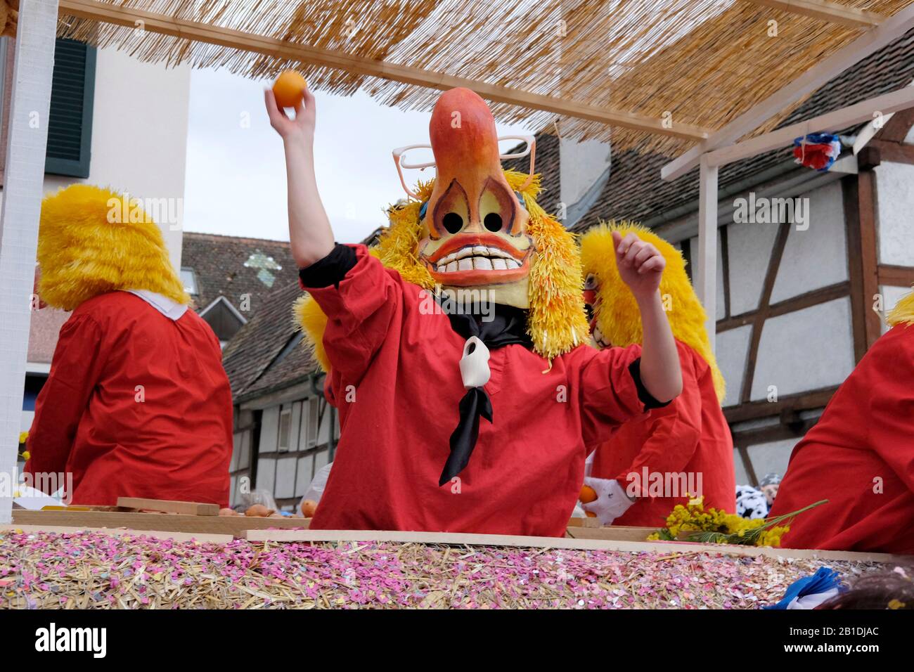 Ein Teilnehmer mit Maske wirft dem Publikum beim Baseler Karneval eine Orange Stockfoto