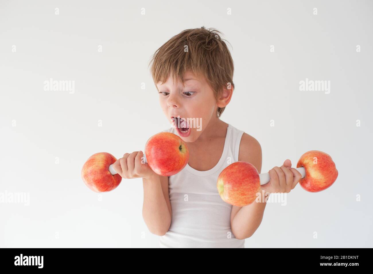 Hungrig aktiv starkes kleines Kind in Tanktop mit Hanteln aus apfelfrüchten, die beißen möchten Stockfoto