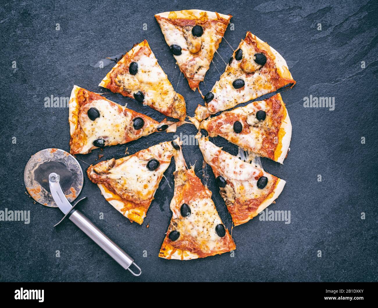 Hausgemachte vegetarische Pizza in Scheiben geschnitten auf Schiefergrund Stockfoto