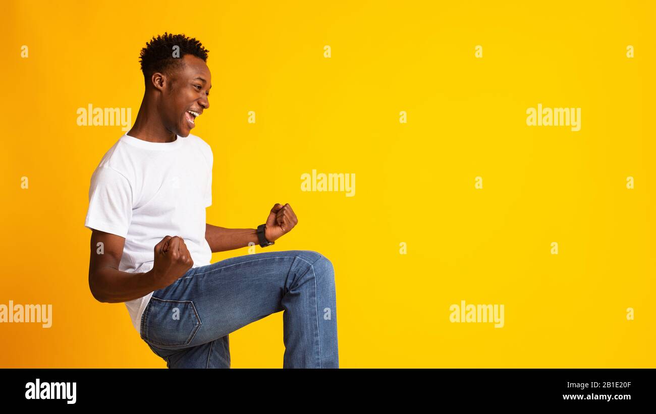 Aufgeregter junger afrikaner, der Erfolg auf Gelb zum Ausdruck bringt Stockfoto