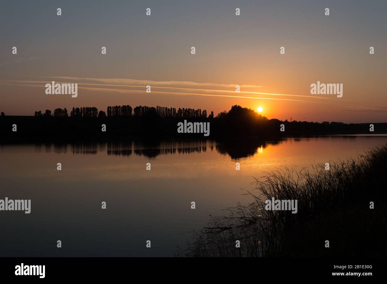 Das Bild der Schallwelle, das von der Silhouette der Bäume und ihrer Reflexion im Spiegel des ruhigen Sees bei Sonnenuntergang gemacht wird. Bäume an einem Seeufer bei Sonnenuntergang. Stockfoto