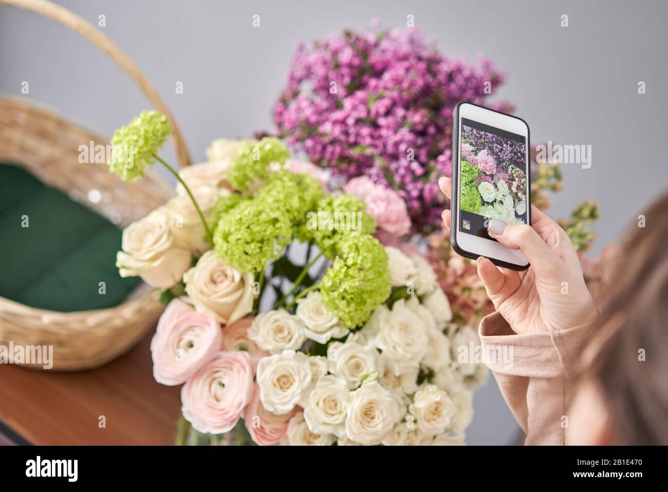Eine Frau macht ein Foto auf ihrem Telefon mit Blumen. Blumengeschäft Konzept . Blumenfrau schafft Blumenarrangement in einem Korbkorb. . Blumen Lieferung. Stockfoto