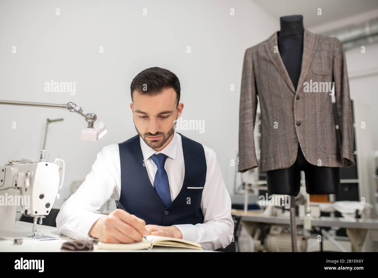 Schneidermännchen sitzt an der Nähmaschine und macht sich Notizen Stockfoto