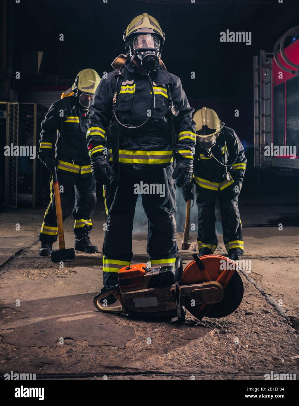 Gruppe von drei jungen Feuerwehrmann, die mit Uniform und Werkzeug in der Feuerwehr posieren Stockfoto