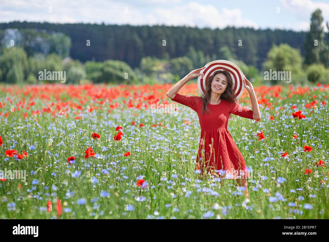 Verträumte Frau im roten Kleid und einem grossen Rot gestreifte Hut in der schönen Kraut blühenden Mohnfeld. Vintage elegant romantisch aussehen. Konzept der schöne Sommer Stockfoto
