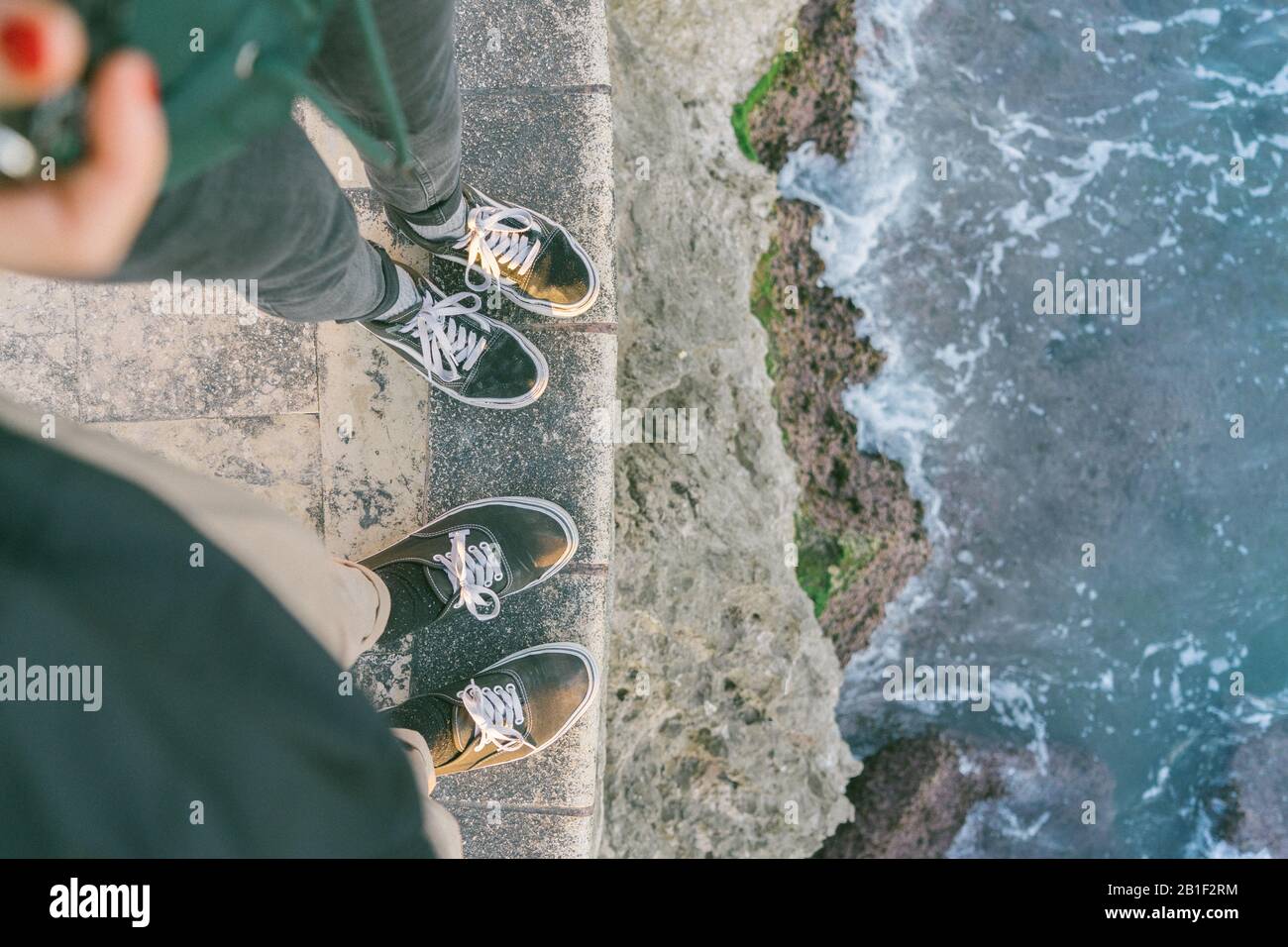 Paar steht neben dem Meer mit passenden Schuhen und abstürzenden Wellen auf Felsen Stockfoto