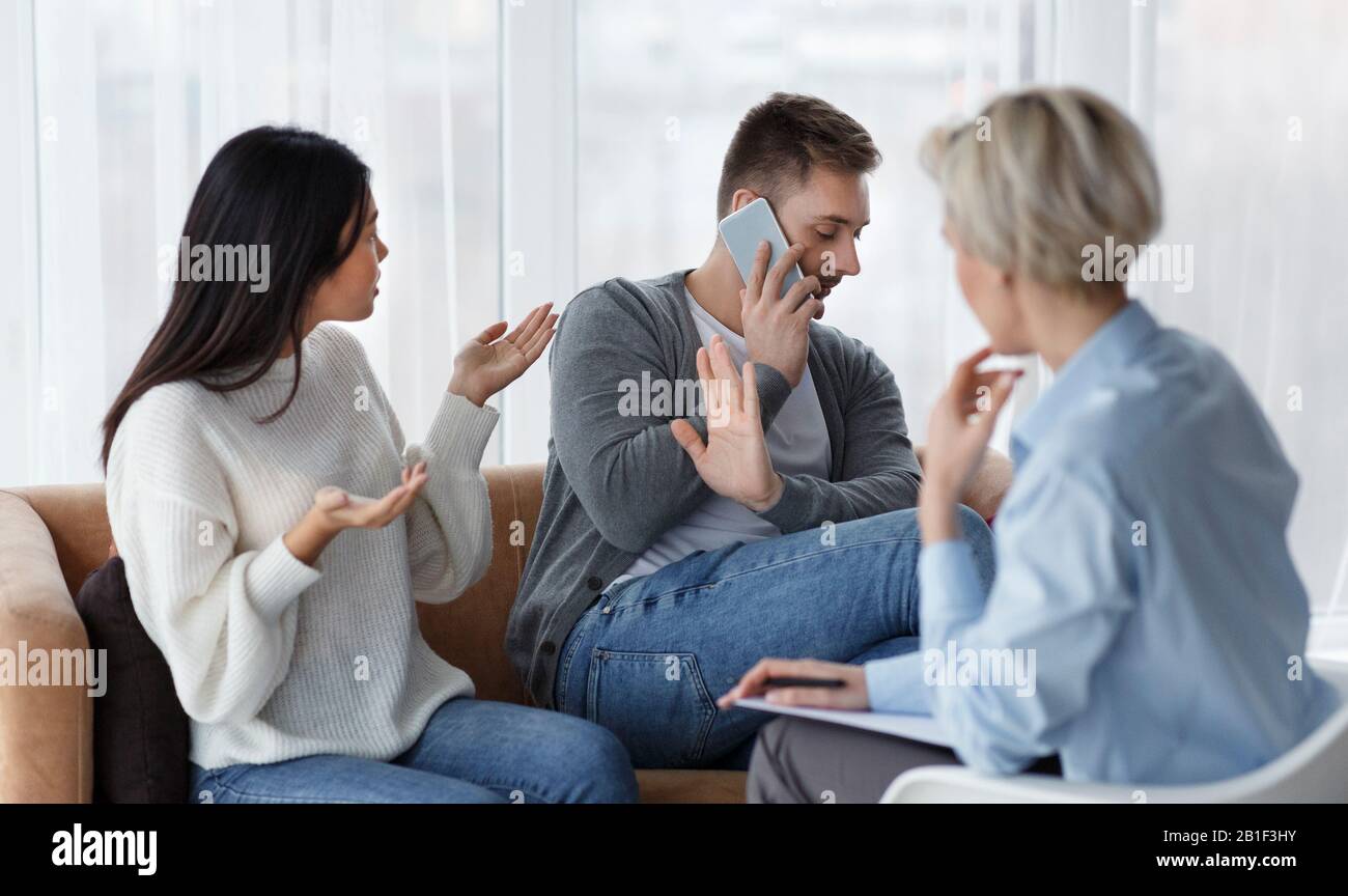 Frau Gibt Dem Ehemann Die Schuld, Er Spricht Auf Dem Handy Im Büro des Beraters Stockfoto