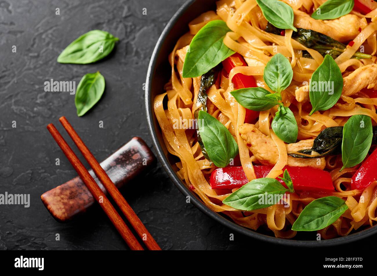 Thailändische Betrunkene Nudeln oder Pad Kee Mao in schwarzer Schüssel mit dunklem Schieferhintergrund. Betrunkene Nudeln sind thailändische Gerichte mit Rice Nudeln, Chicken Meat, Basi Stockfoto