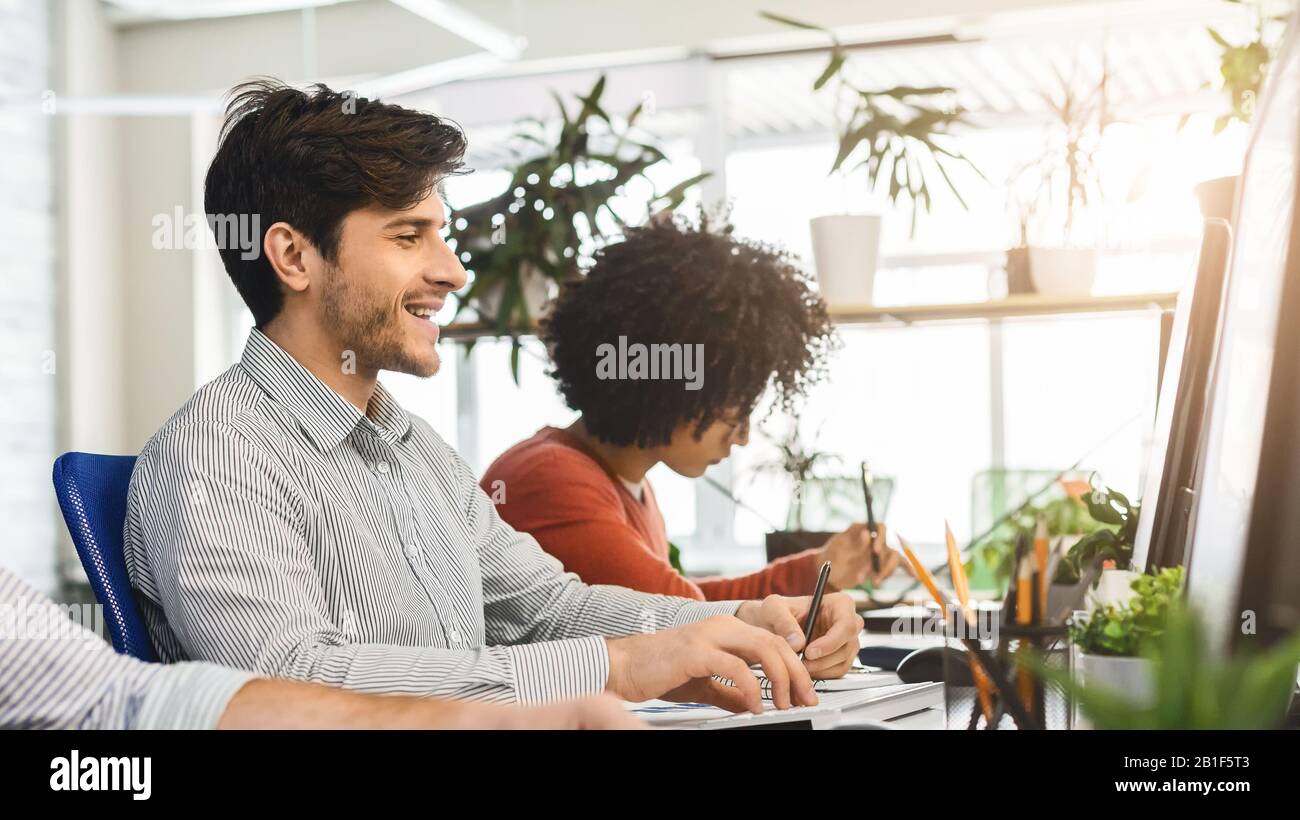 Junger Kerl genießt seinen Job und arbeitet mit Kollegen im Büro Stockfoto