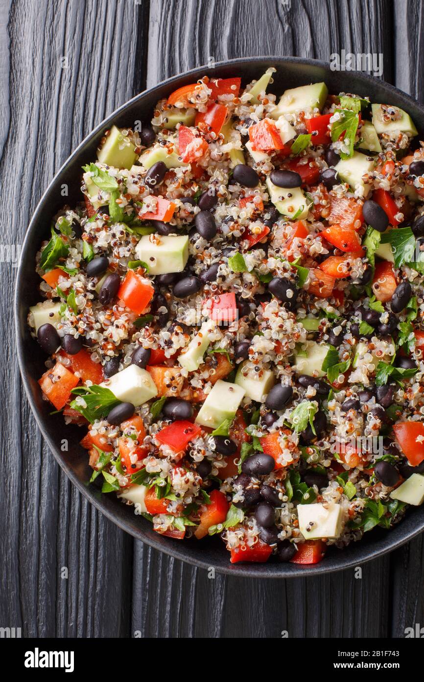 Gekochtes Quinoa mit frischen Avocado, Paprika, Tomaten und schwarzen Bohnen in einem Teller auf dem Tisch. Vertikale Draufsicht von oben Stockfoto