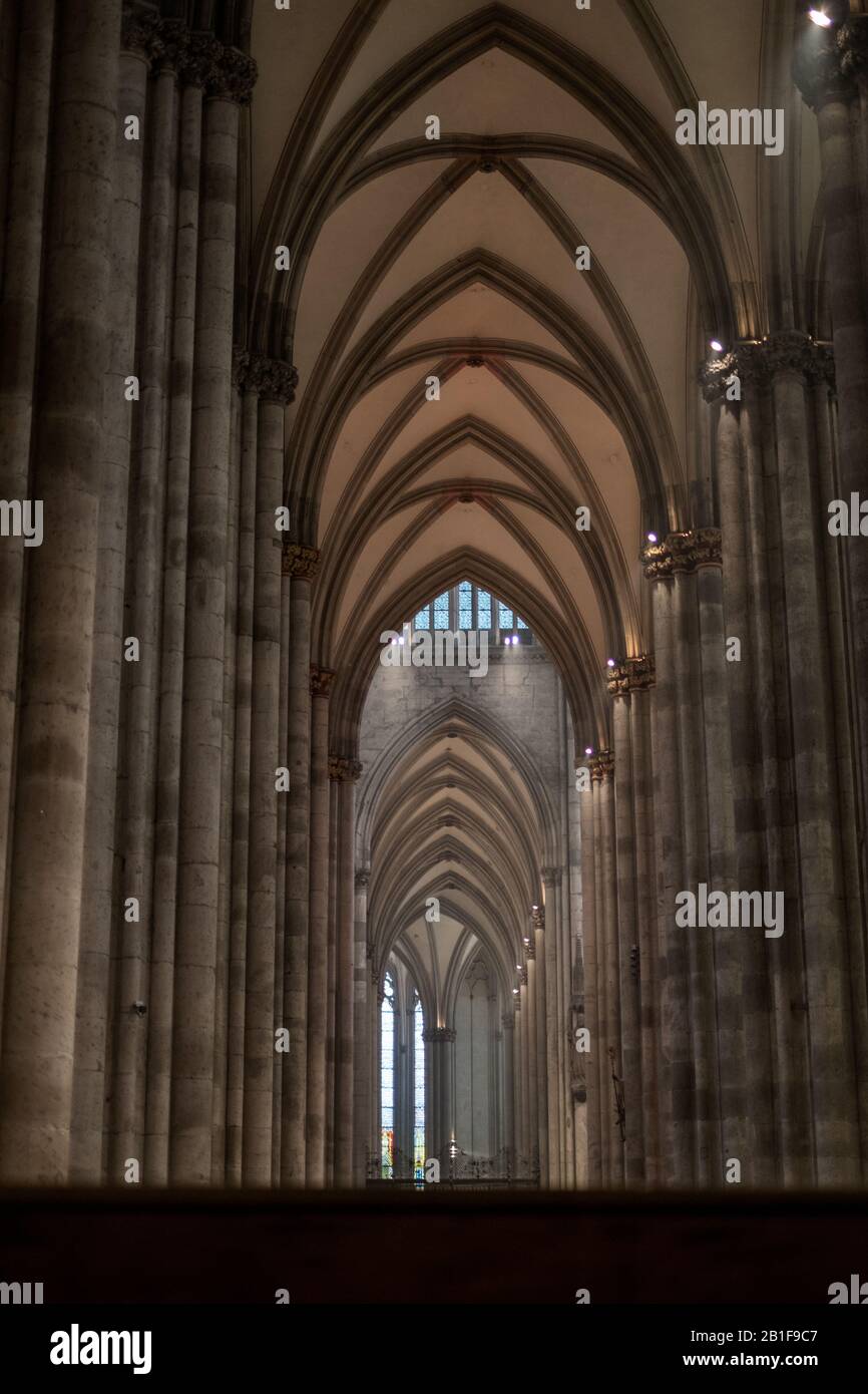 Hohe Säulen und schöne Gewölbe bilden einen Gang im Kölner Dom. Es zeigt die Unermesslichkeit, die Höhe und die Länge des Innenraums. Stockfoto
