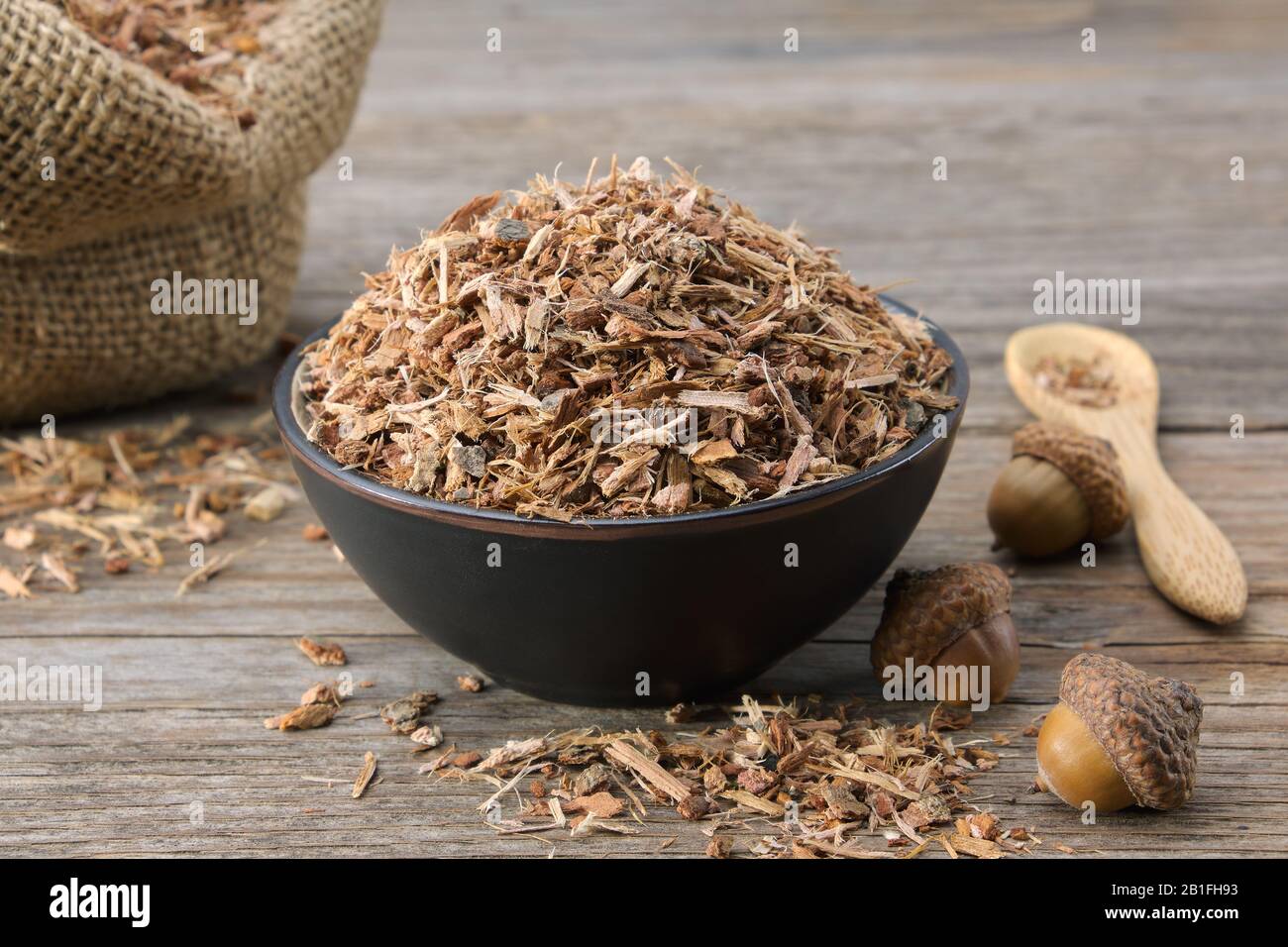 Gesunde Eiche Rinde in schwarzer Keramikschale und Eicheln auf Holztisch. Pflanzenheilkunde. Stockfoto