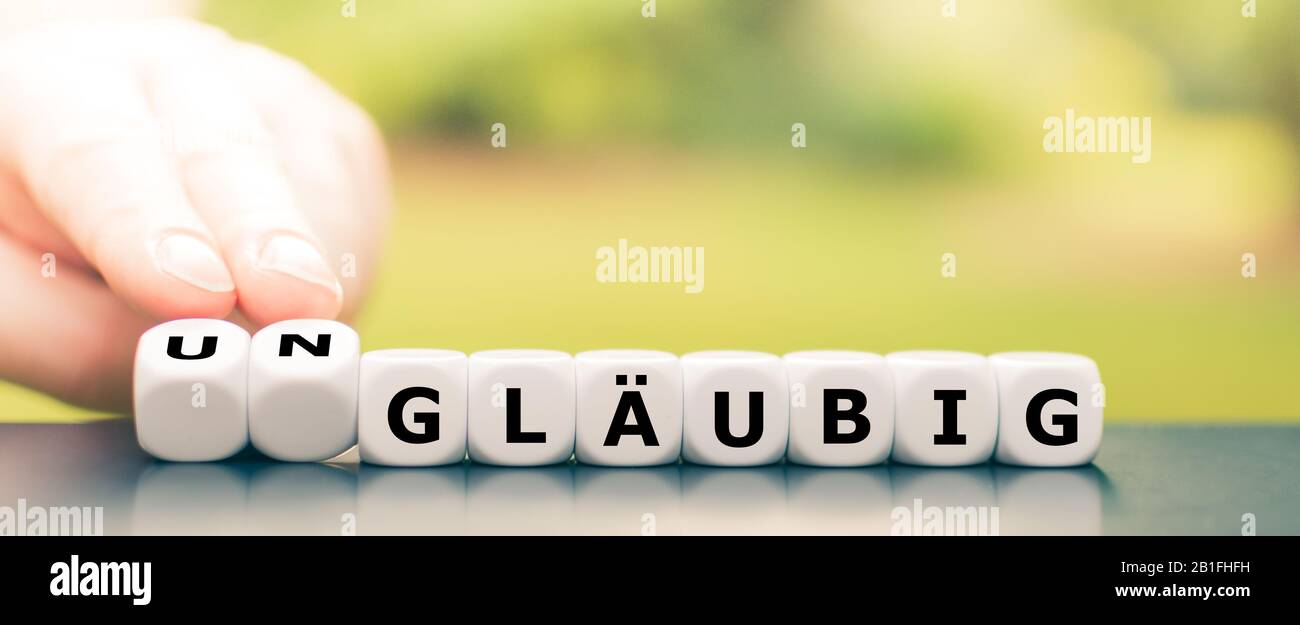 Hand dreht Würfel und ändert das deutsche Wort "gläubig" (religiös) in "ungläubig" (irreligiös). Stockfoto