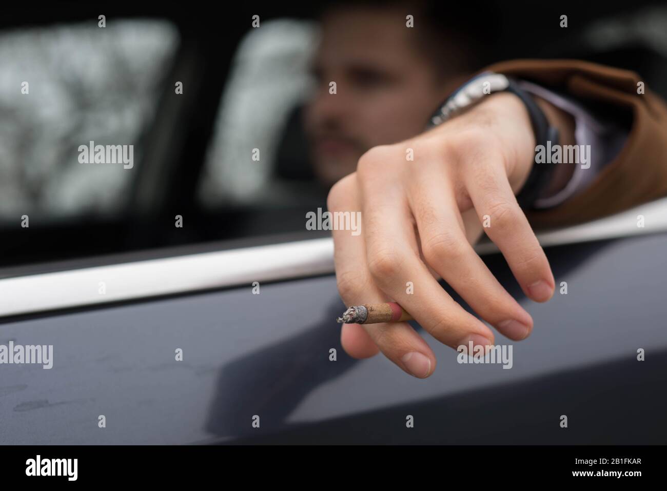 Porträt eines jungen Mann, 30 Jahre alt, aus der Nähe, Autofahren, raucht eine Zigarette. Geschäftsmann mit Bart in einem Anzug, raucht brutal ein Stockfoto