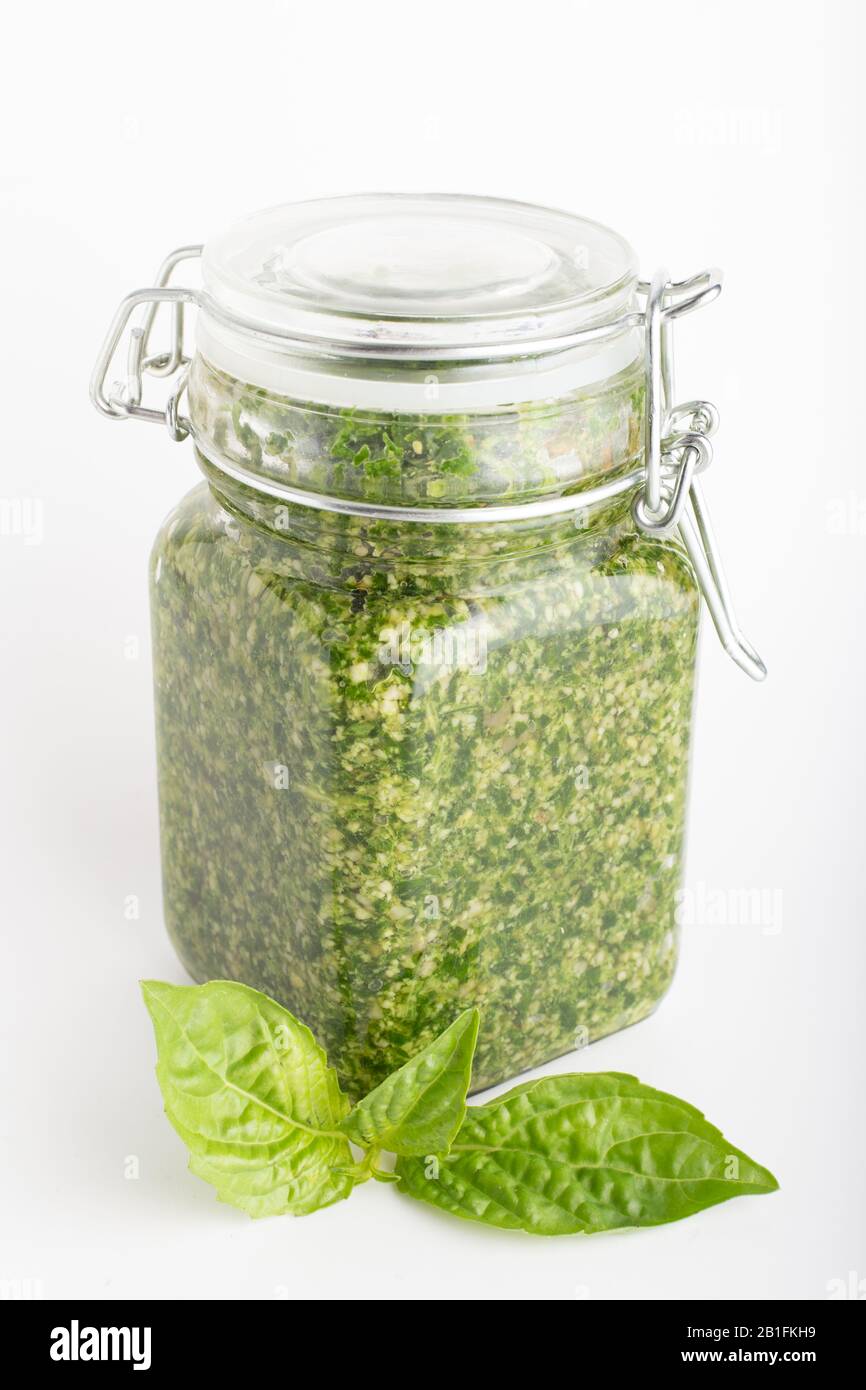 Pesto in einem Glasbecher, isoliert mit frischen Basilikumblättern auf weißem Hintergrund. Traditionelle hausgemachte italienische Soße Pesto und Basilikum. Stockfoto