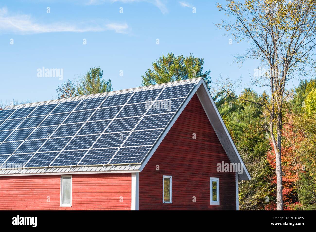 Dach einer traditionellen roten, amerikanischen Holzscheune, die an einem sonnigen Herbsttag mit Solarpaneelen bedeckt ist Stockfoto