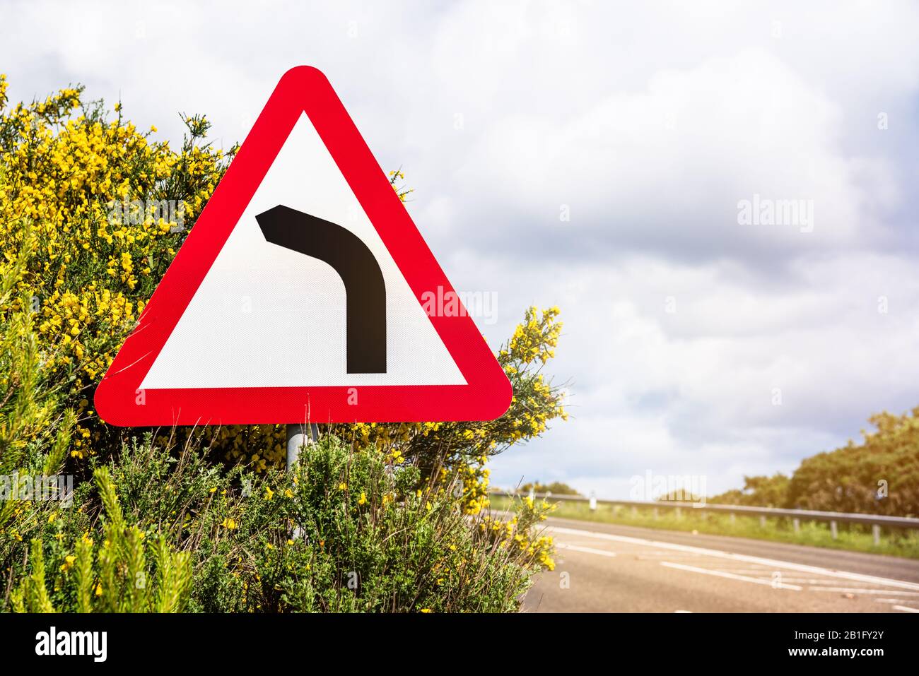 Gefährliche Kurve vor dem Warnschild auf einer Küstenstraße an einem sonnigen Frühlingstag Stockfoto
