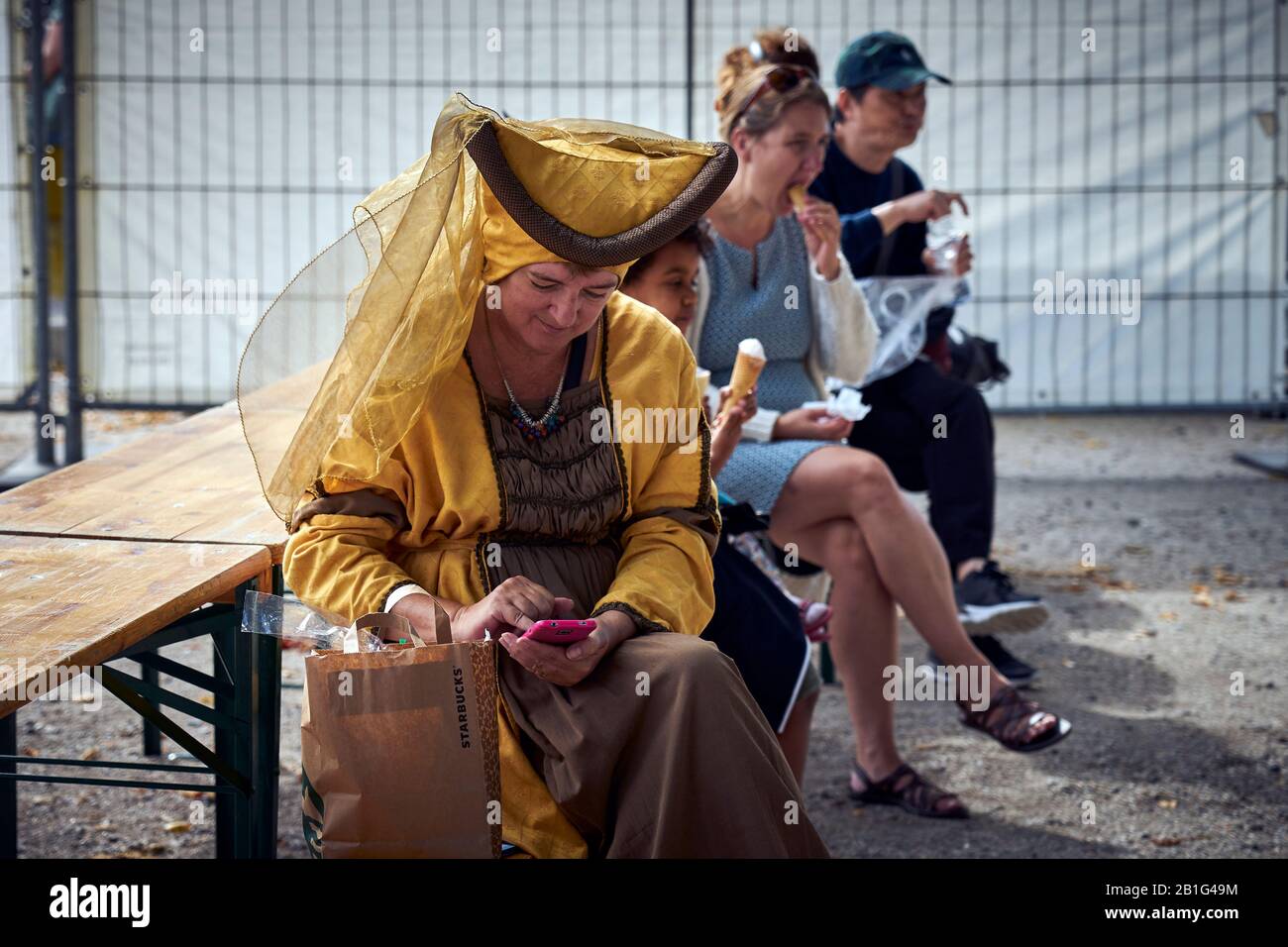 Eine Frau, die in mittelalterlichen Kostümen gekleidet ist, sieht ihr Telefon während einer Pause von der Veranstaltung an Stockfoto Eine Frau, die in mittelalterlichen Kostümen gekleidet ist, sieht ihr Telefon während einer Pause von der Veranstaltung an Stockfoto