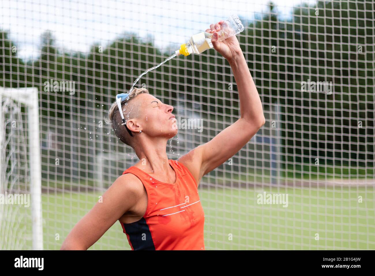 Eine Sportfrau trinkt Wasser und schüttete Wasser auf sie. Stockfoto