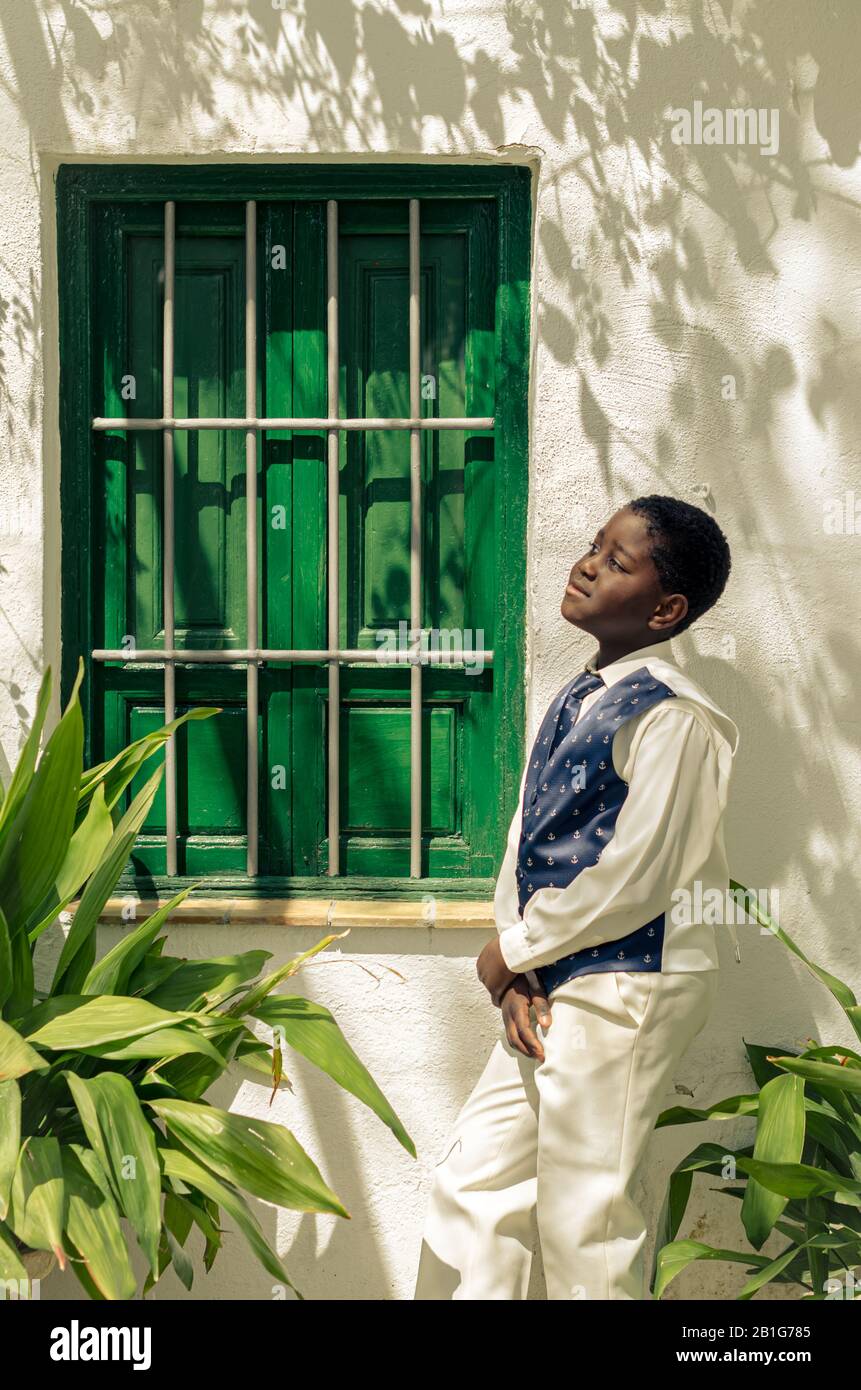 Schwarzer Junge mit weißem Hemd und blauer Krawatte neben einem grünen Fenster Stockfoto