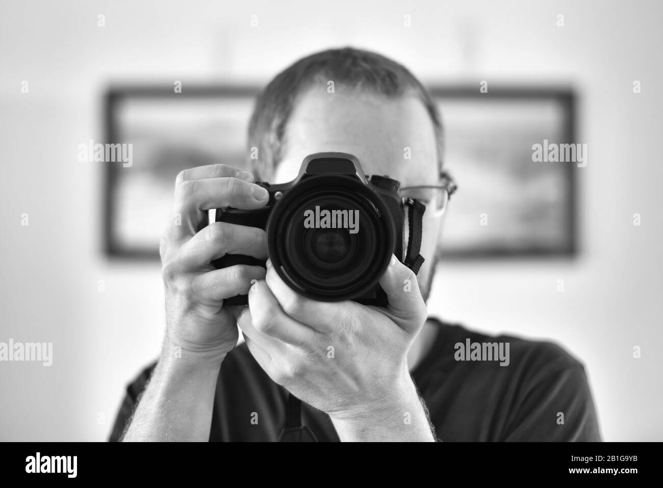 Selbstporträt durch einen Spiegel eines nicht erkennbaren kaukasischen Mannfotografen, der eine Kamera hält (Fokus auf Kameralinse). Stockfoto