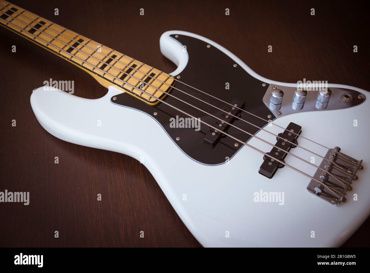 White Electric Bass Gitarre mit Maple Neck, Black Pickguard und Black Block Inlays auf einem Einfachen Holzhintergrund Stockfoto