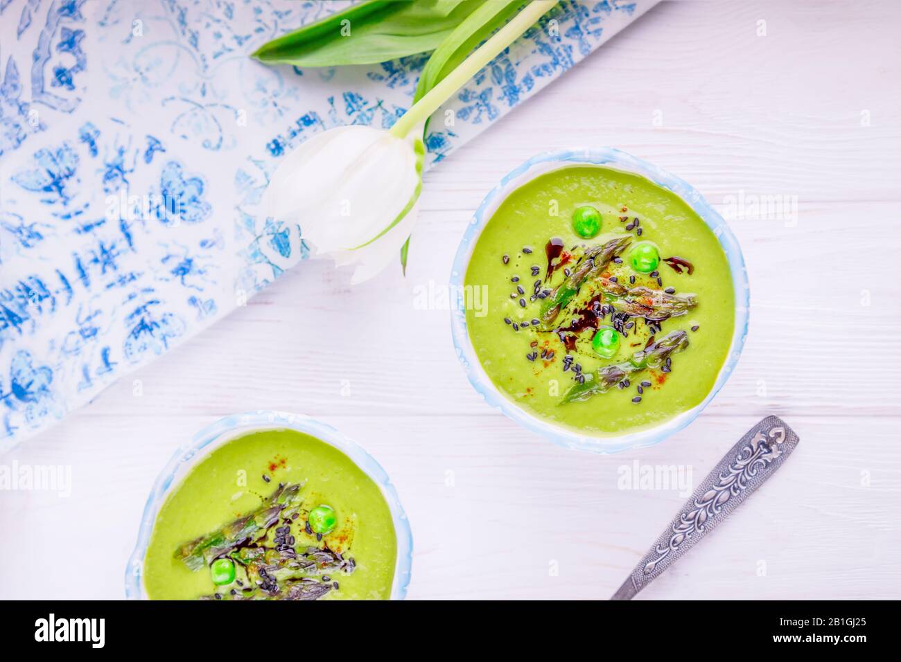 Spargelsaison. Hausgemachte grüne Sahnesuppe mit Spargel, grünen Erbsen, schwarzen Sesamsamen und Kürbisöl auf weißem Grund Stockfoto