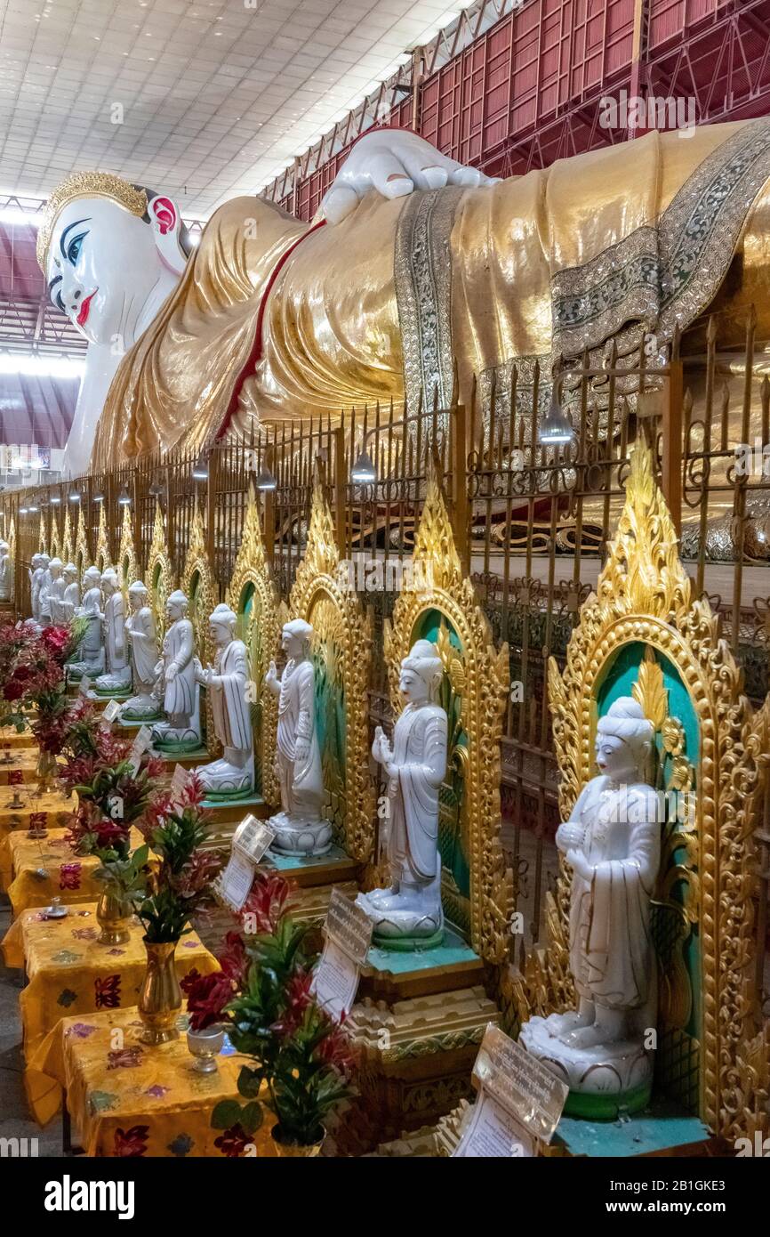 Eine Reihe buddhistischer Schreine, die die riesige Statue des sich zurücksetzenden Buddha in Chaukhtatgyi Paya, Yangon, Myanmar, umsäumen Stockfoto