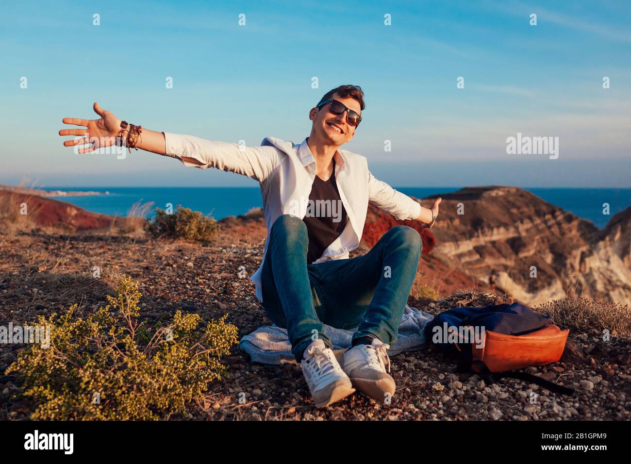 Touristen Wanderer, die auf der Bergkuppe am Meer auf der Insel Santorini Spaß haben und die Landschaft genießen. Glücklicher Mann öffnete die Arme auf Reisen Stockfoto