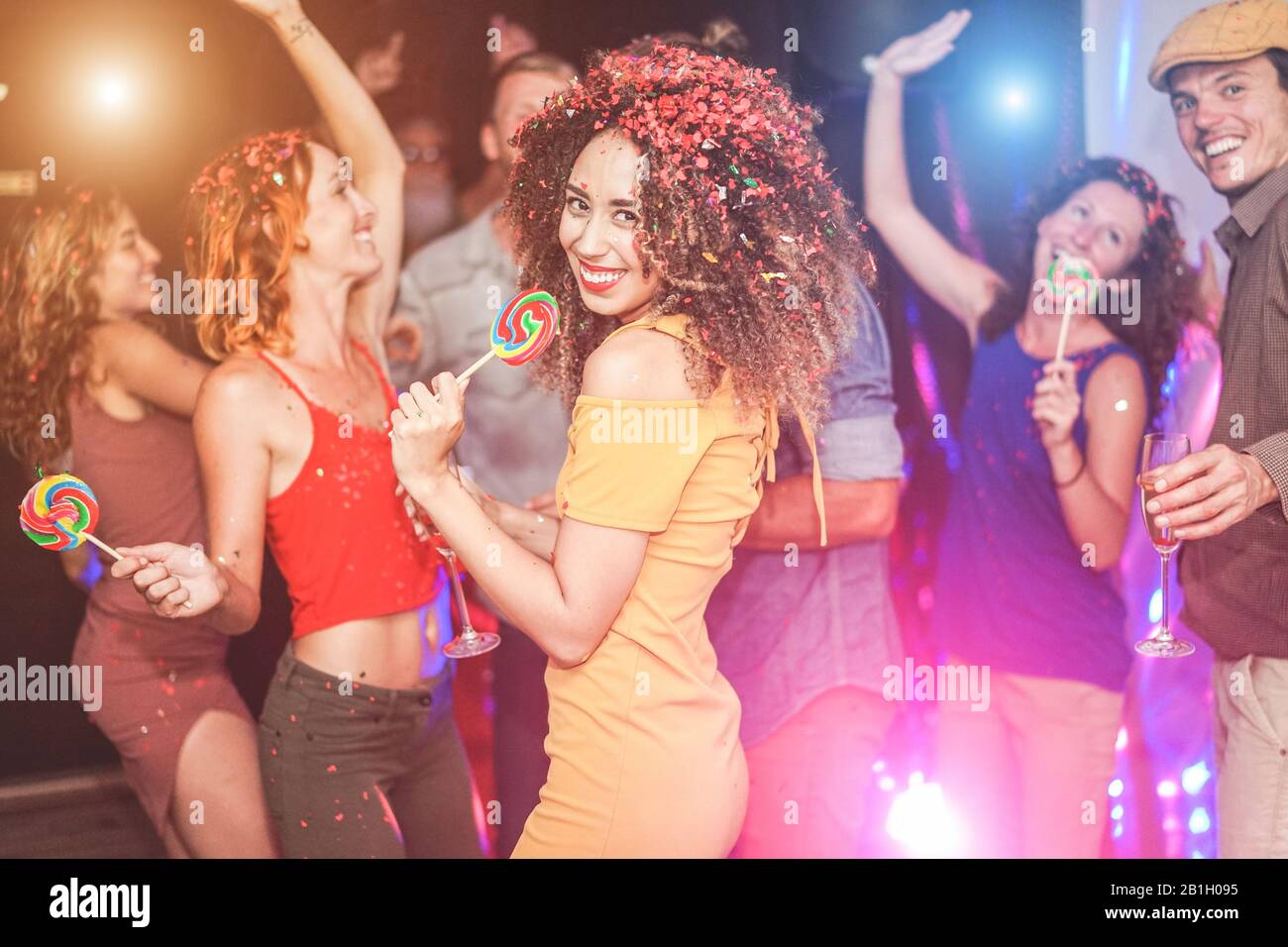 Fröhliche Freunde, die auf der traditionellen Nachtparty mit Konfetti, Champagner und Süßigkeiten Lollipop tanzen - Trendige junge Leute, die Spaß im Nachtclub haben - Jugend und Stockfoto