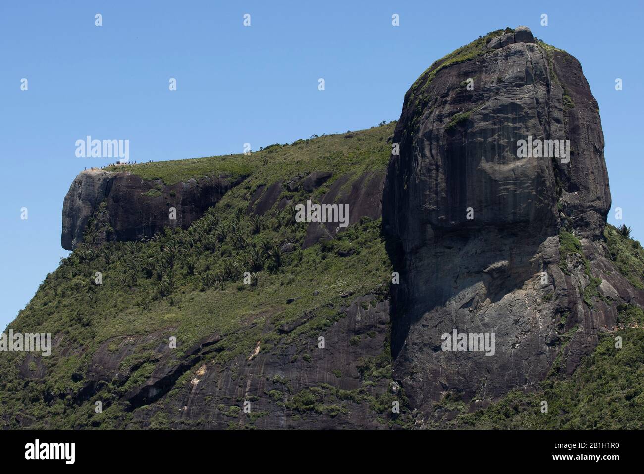 Gavea Rock mit Emporen Kopf in Rio de Janeiro mit Menschen winzig auf dem Grat vom Aussichtspunkt Pedra Bonita aus gesehen gegen einen klaren blauen Himmel Stockfoto