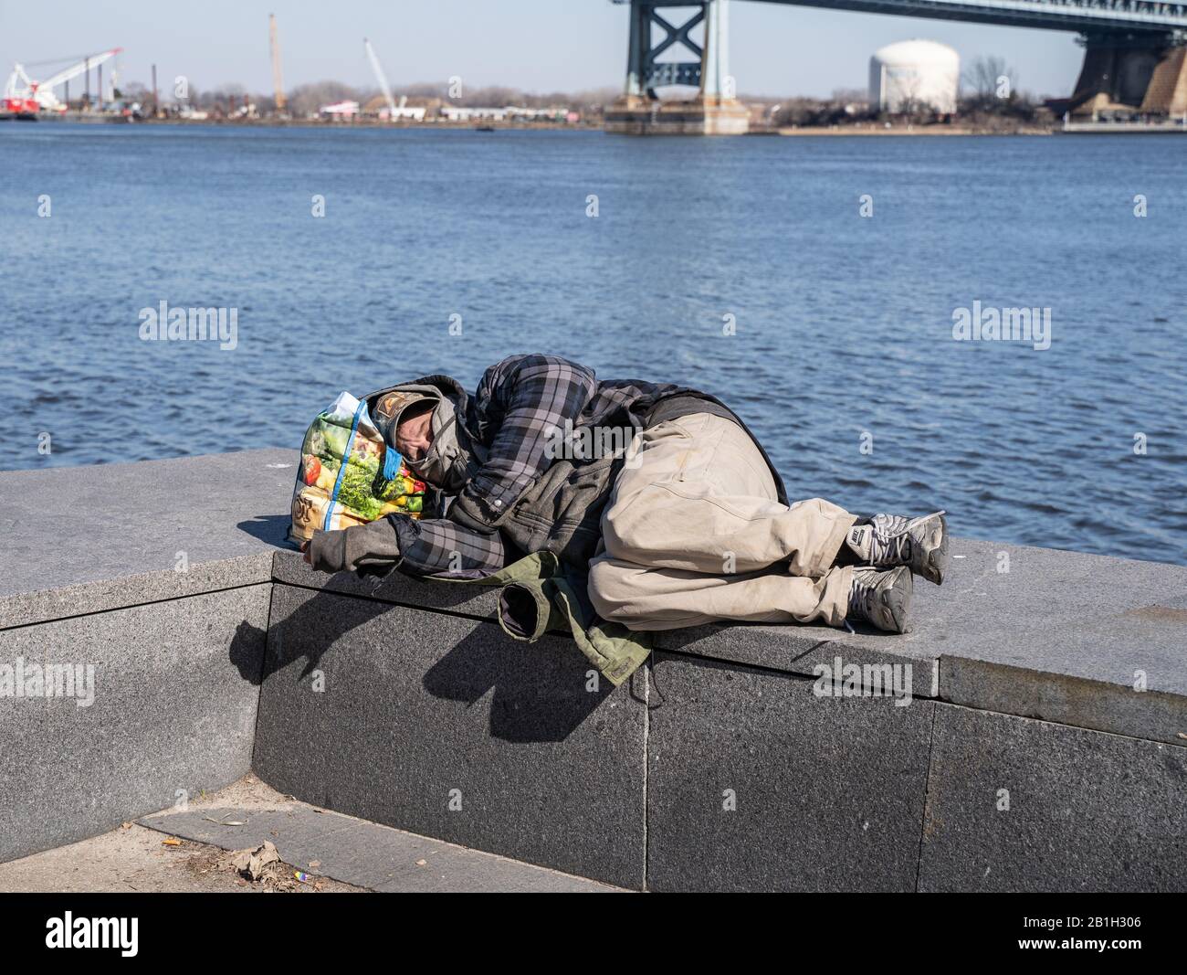 Philadelphia Pennsylvania, 23. Februar 2020: Ein obdachloser Mann schläft auf einer Steinbank entlang der Uferpromenade bei Penn's Landing Stockfoto