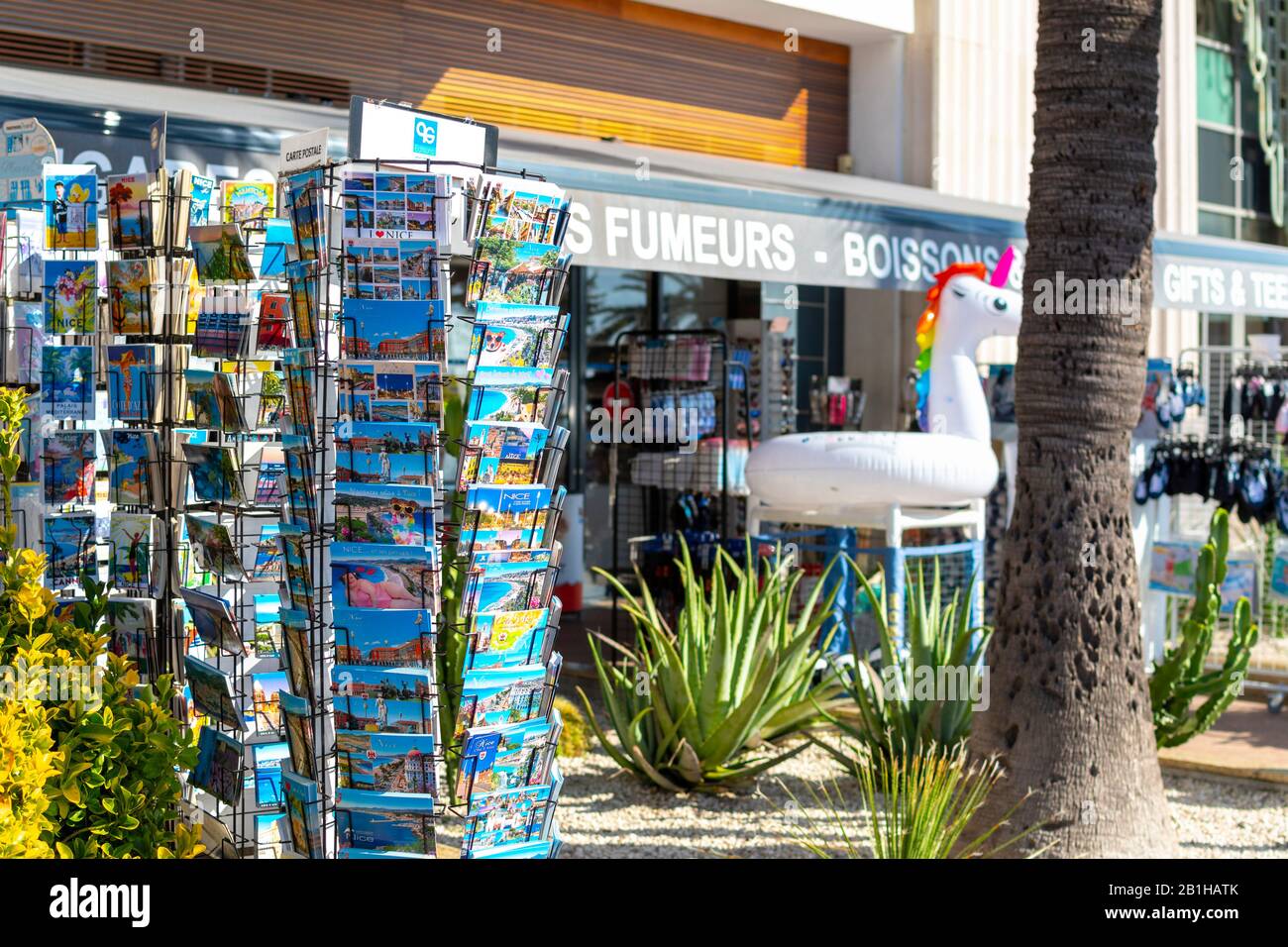 Ein Postkartenregal steht in selektivem Fokus mit einem Souvenirladen, der hinter der Strandpromenade des Mittelmeeres in Nizza, Frankreich, verschwimmen wird. Stockfoto