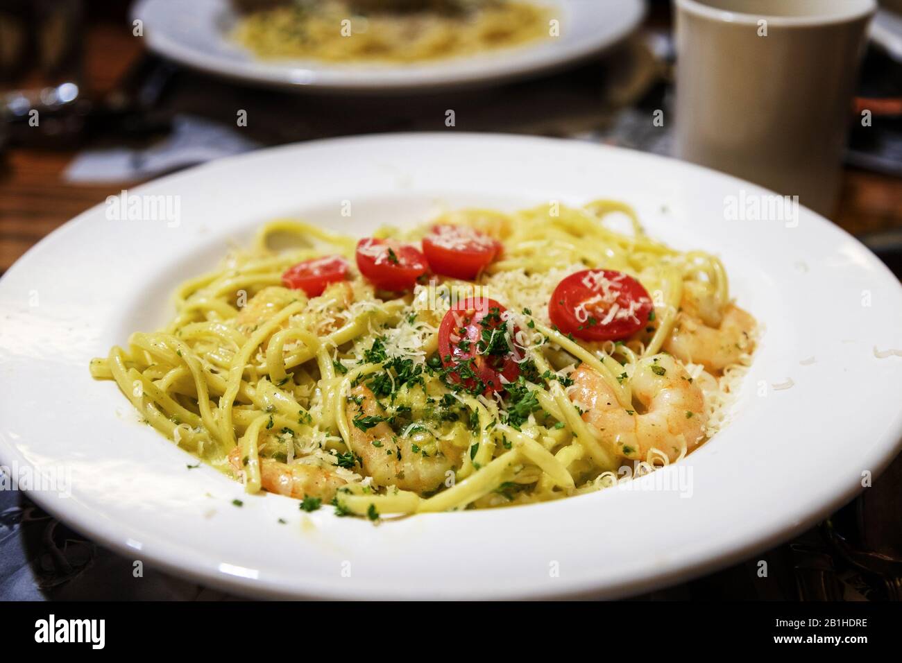 Hausgemachtes Pesto linguine mit sautierten Garnelen, gemischt mit biologischem Basilikum, Piniennüssen und Mandeln, die in Alfredo Sauce gemischt und mit Traubentomaten garniert wurden Stockfoto