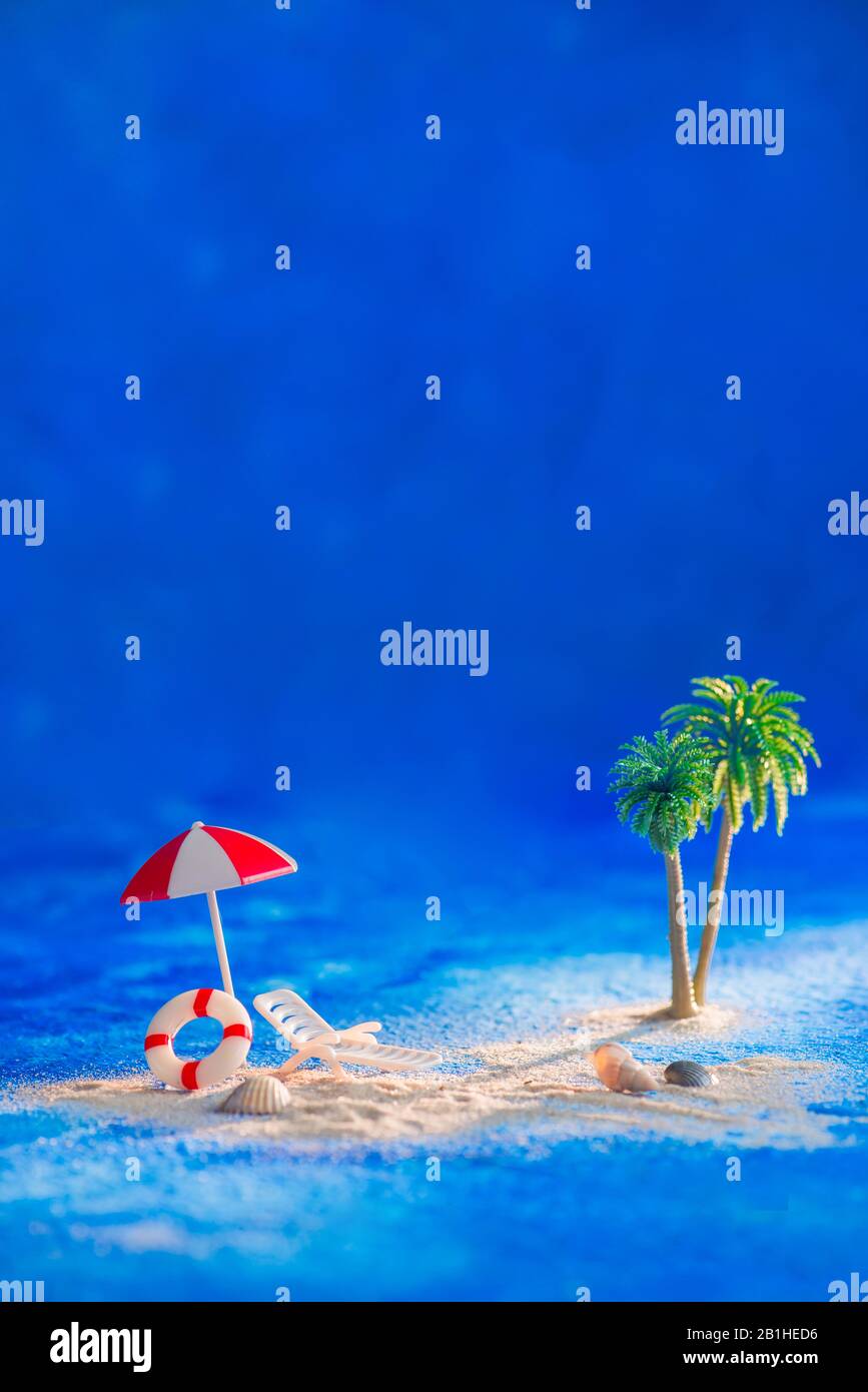 Figürliche Strandszene im Sommer, Spielzeugpalmen, Regenschirm und Liegestuhl auf blauem Hintergrund mit Kopierraum Stockfoto