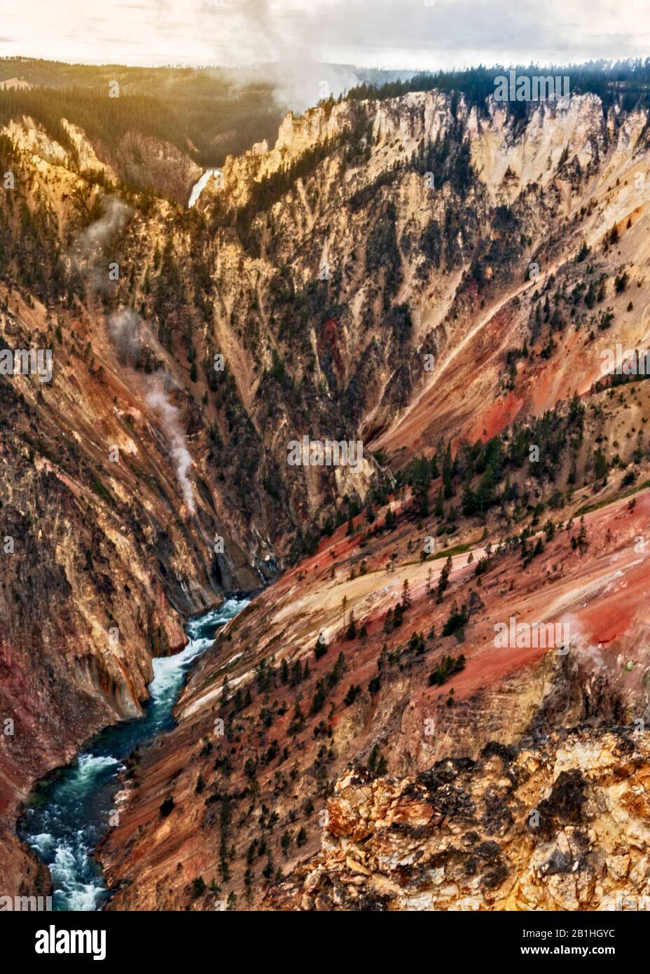 Tiefer Canyon mit farbenfrohen orangefarbenen, roten und gelben Wänden, frühmorgendlicher Sonnenaufgang und tief am unteren Rand des Canyons mit grünem Wald auf Höhe von m. Stockfoto