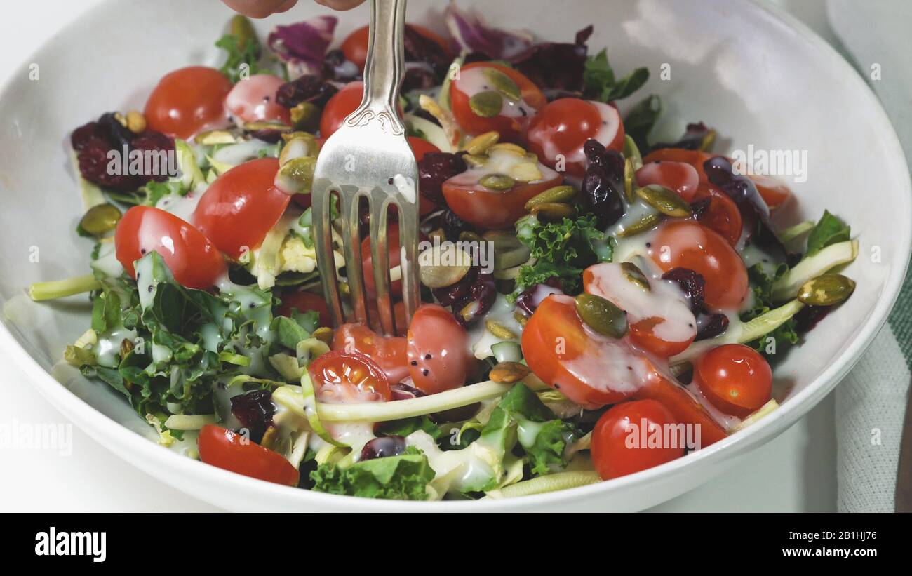 Gemüsesalat aus grünen Blättern, Tomaten, Kürbissamen, getrockneten Preiselbeeren und Dressing auf einem Teller in der Nähe. Stockfoto