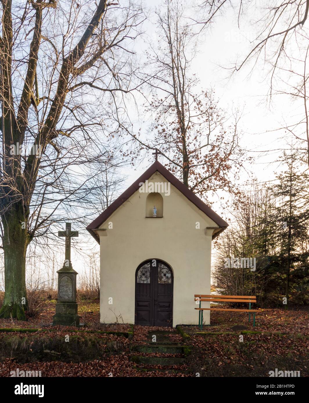Kleine Kapelle mit älterem Steinkreuz, Holzbank und Bäumen in der Nähe des Dorfes Cermna ve Slezsku in Tschechien Stockfoto