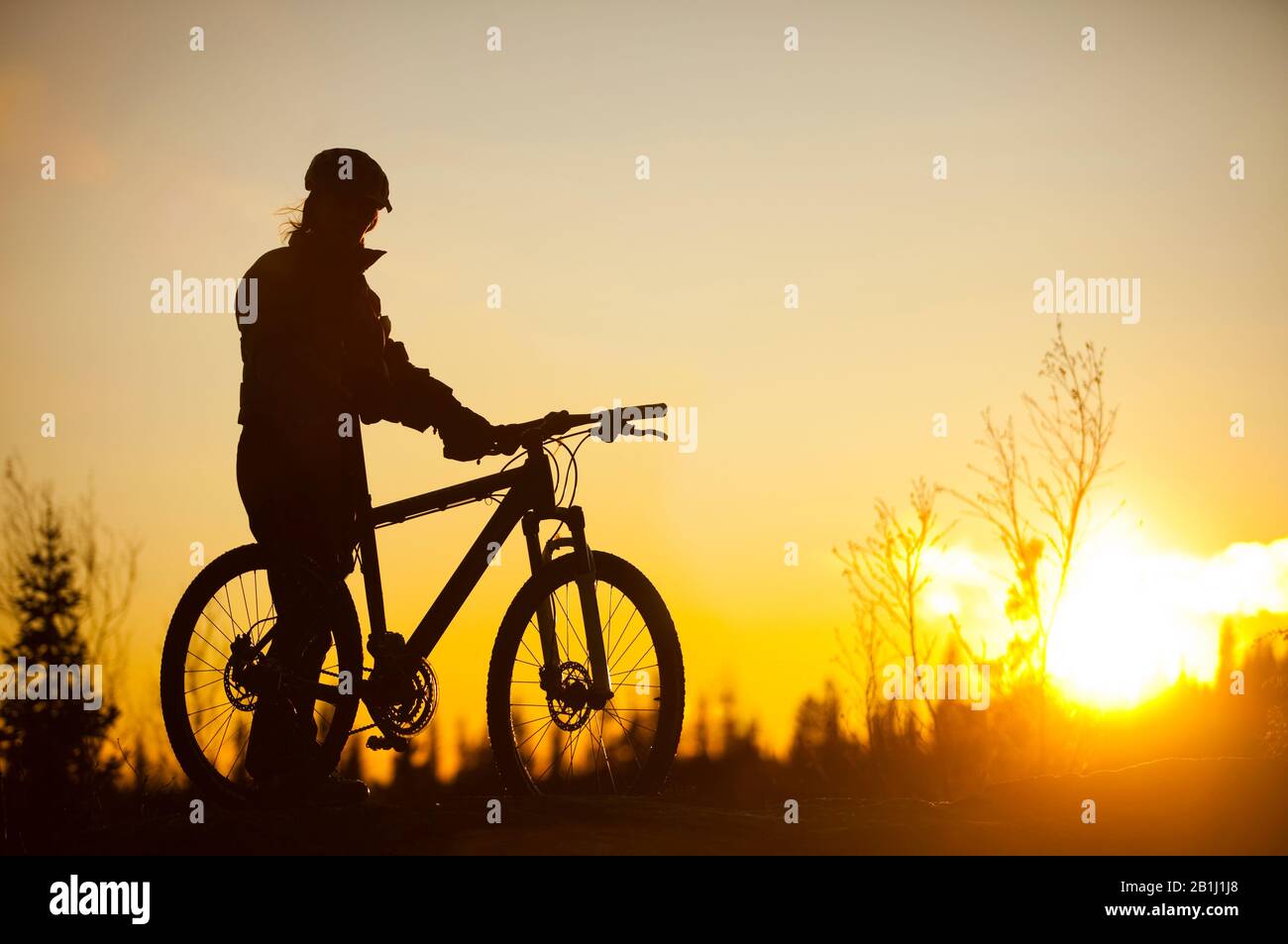 Mann steht mit einem Fahrrad in Silhouette vom Sonnenuntergang Stockfoto